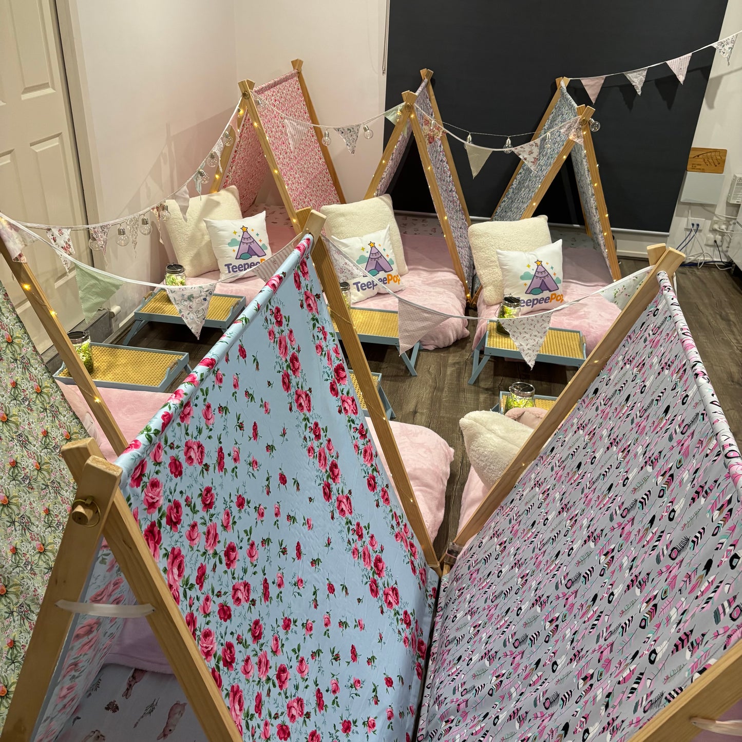 Six (6) colourful cute teepees with bunting, pink blanket, and twinkle lights set up for a luxury indoor slumber party in Melbourne
