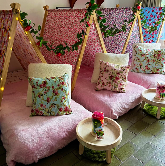 Floral-themed teepee party setup with pink and purple colors, floral pillows, and flowers for the ultimate glamping party experience for kids and girls.